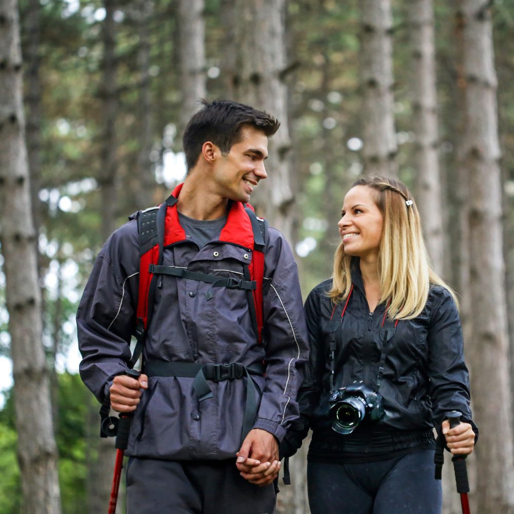 Two people hiking in a forest, wearing outdoor gear.