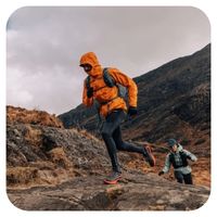 Two hikers on a mountain trail with one wearing an orange jacket.