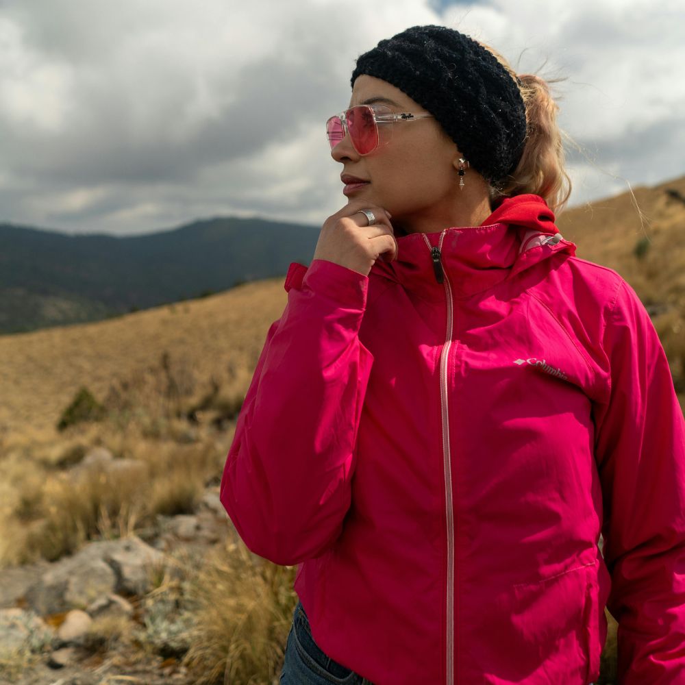 Person wearing a bright pink jacket and black headband standing in a mountainous landscape.